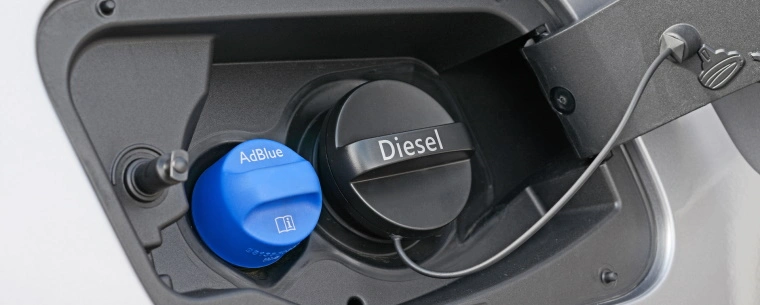 The fuel cover of a silver car is open and there is a diesel cap and a blue AdBlue cap.