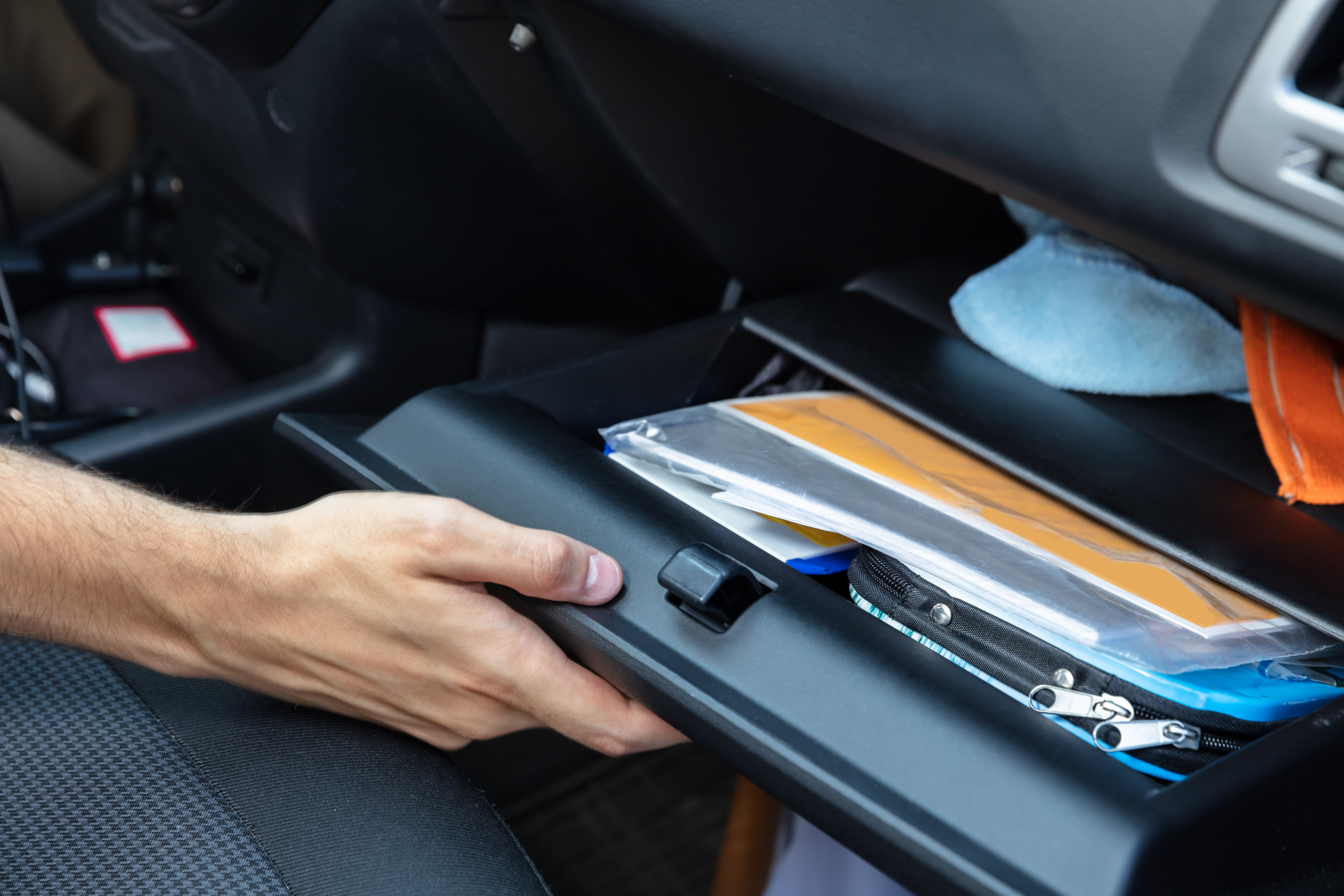 A person holds open the glovebox of a car, which contains documents and file holders.