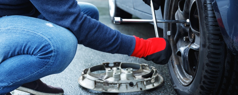 Person using a wheel wrench to loosen wheel nuts on a wheel.
