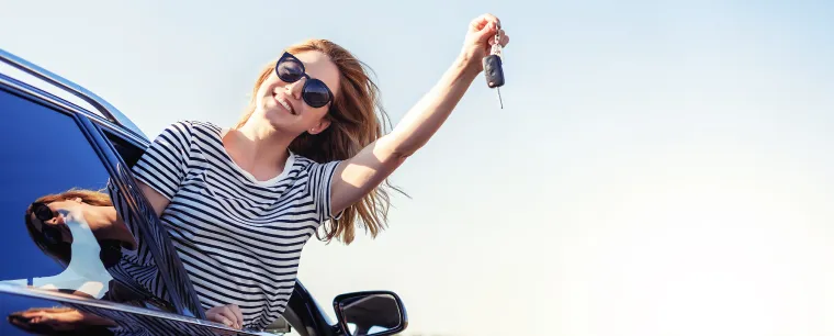 Woman wearing sunglasses hanging out the window of a car dangling her car keys 