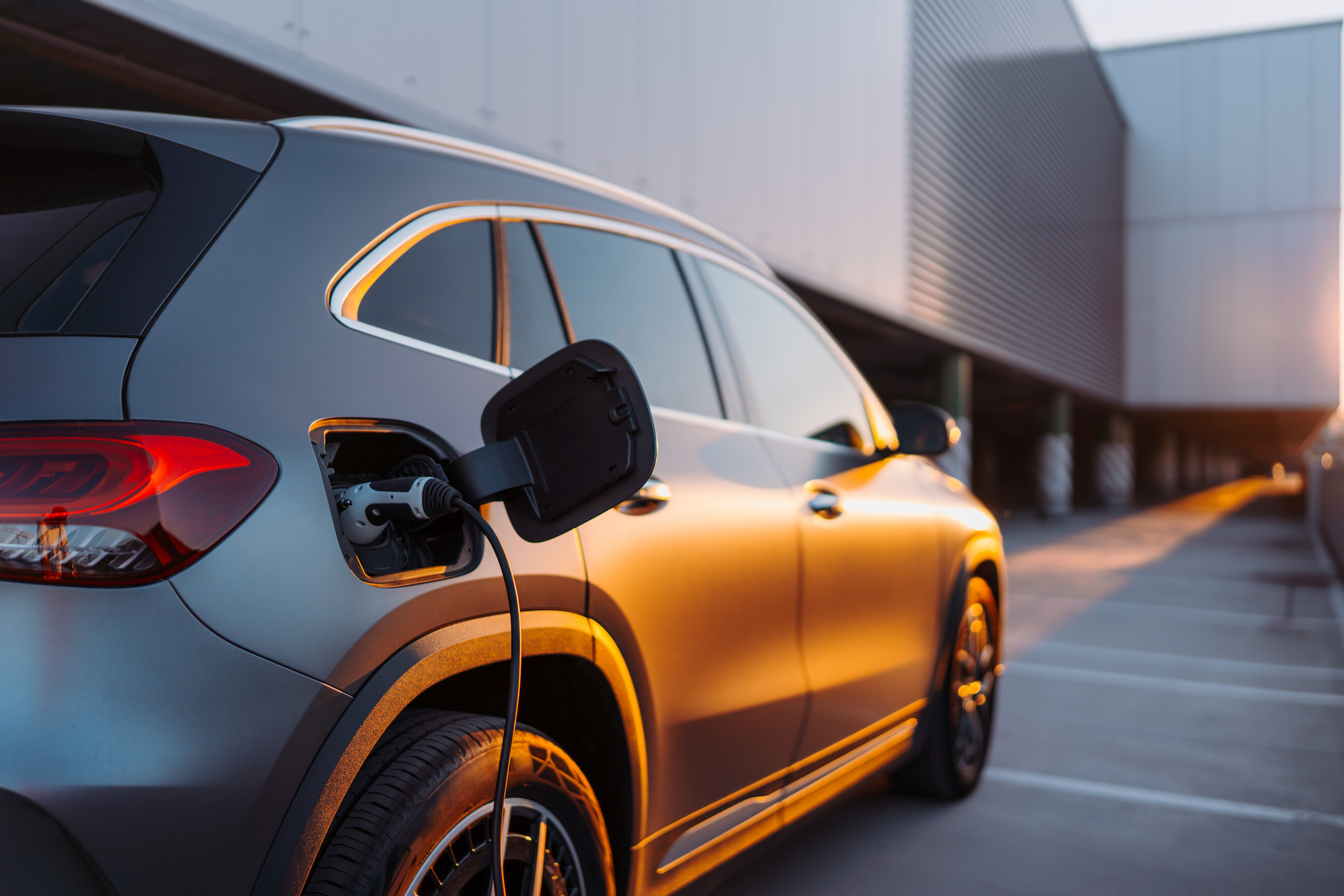 At sunset, a grey electric car is being charged in a car park.