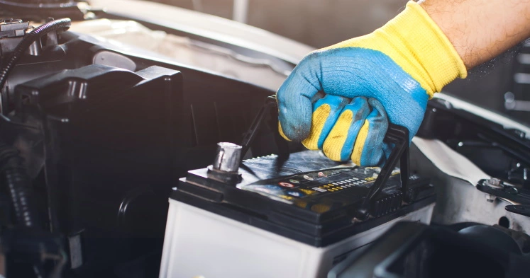 Car mechanic lifting up an electric car battery in the bonnet of an electric car