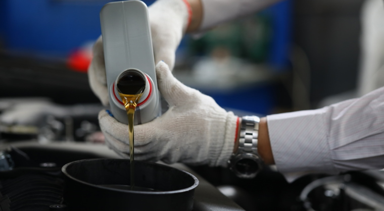 Car mechanic pouring oil into a car's engine.