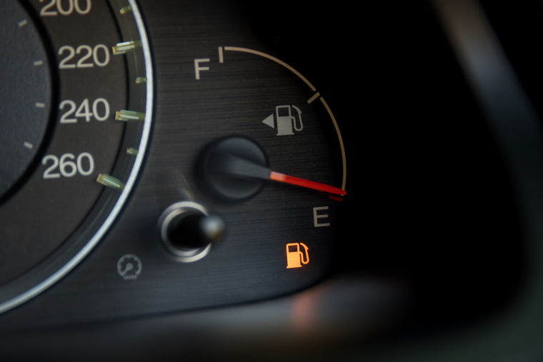 A car's dashboard fuel light shows orange to indicate a lack of petrol.
