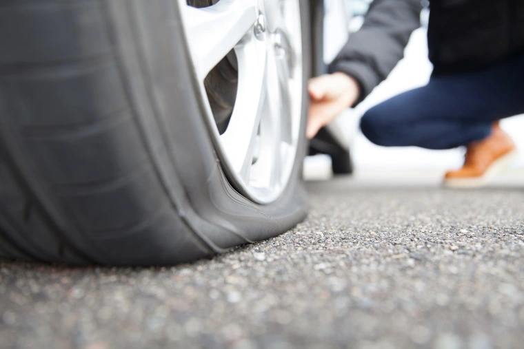 Man kneeling down holding a flat tyre.