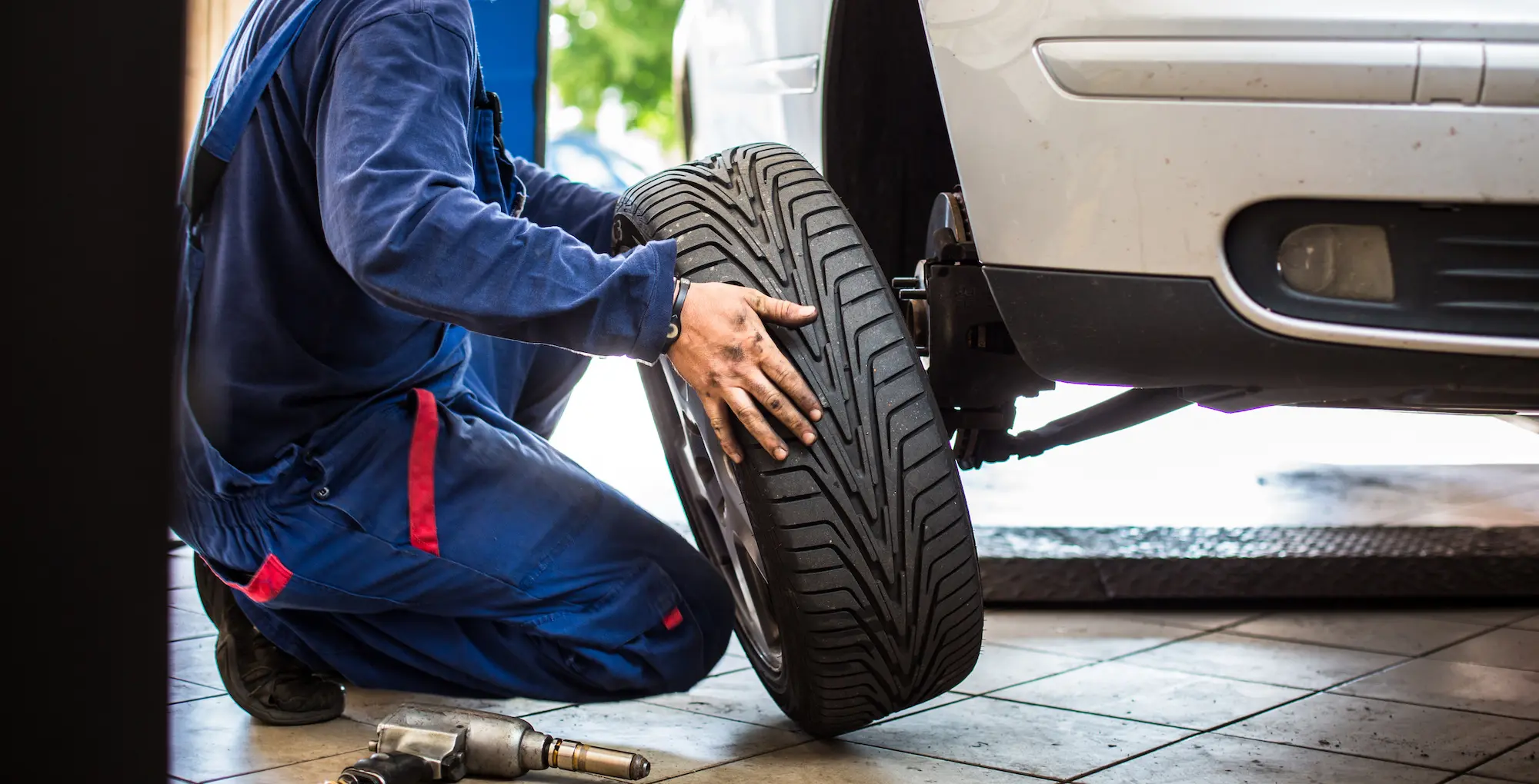 A mechanic kneels on the floor and changes a car's tyre.