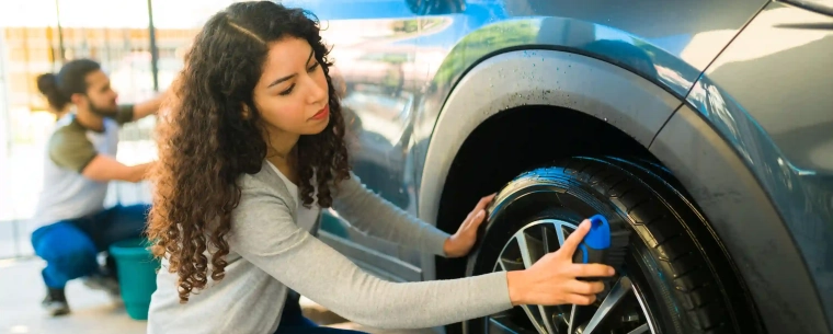 Two people cleaning the tyres on their car.