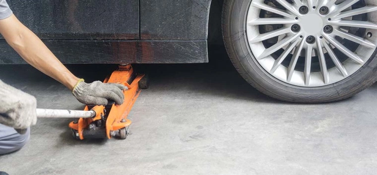 Low profile trolley jack being wheeled underneath jacking point of a car.