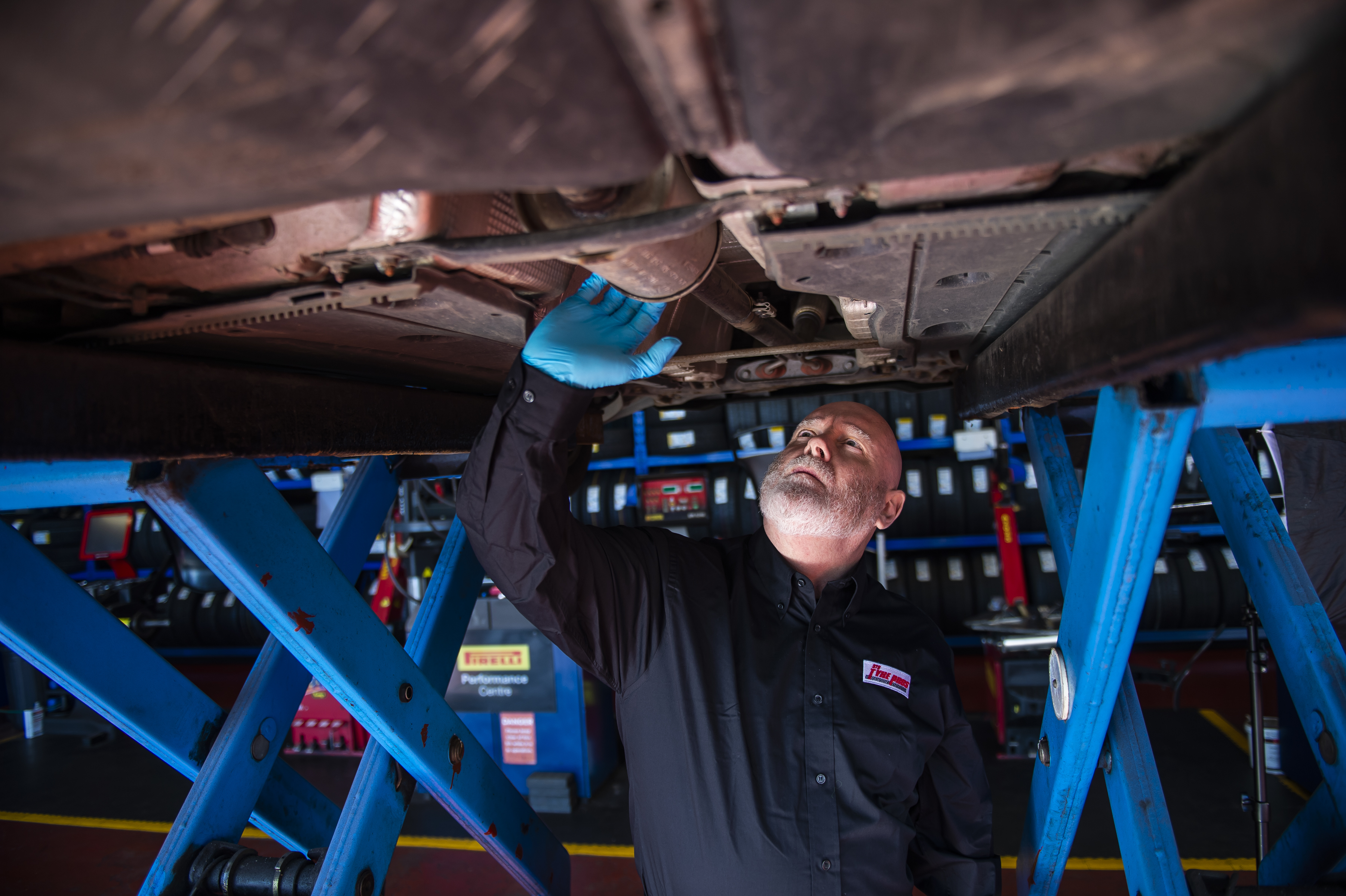 Tyre Pros technician underneath a car lifted by a ramp, checking the exhaust.