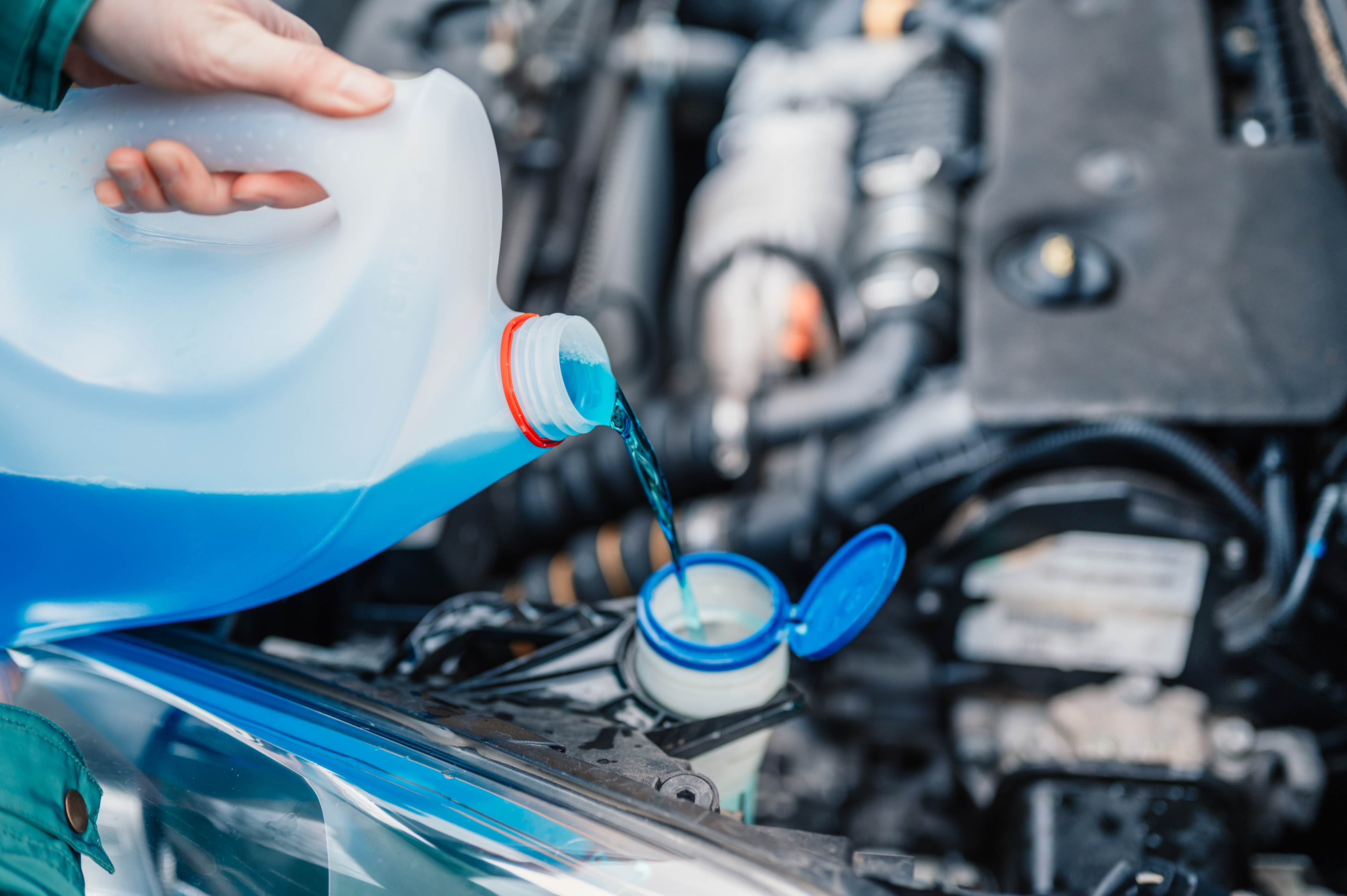 A driver tops up the windscreen wiper fluid reservoir of their car.