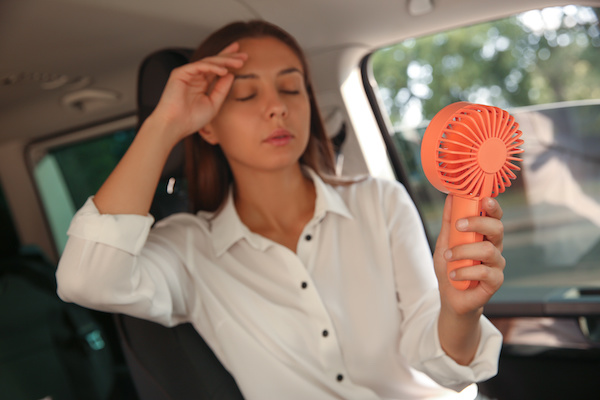 A woman uses a handheld fan to keep her cool inside her car.