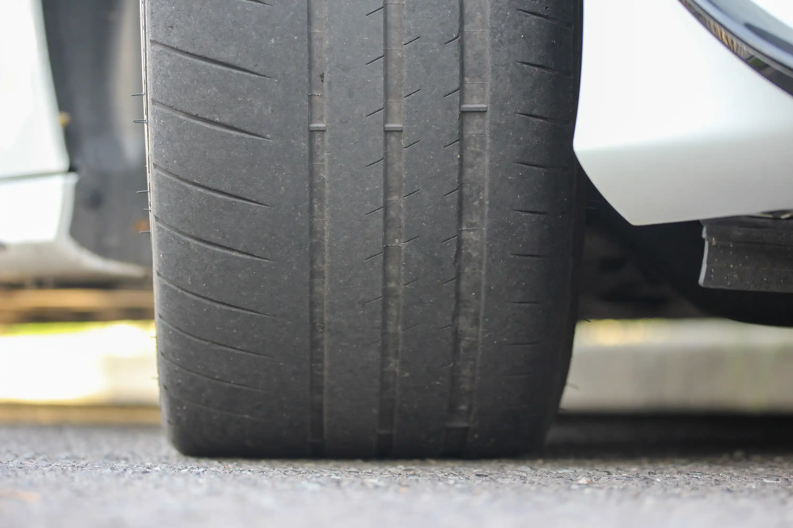 A worn down low profile tyre on a white car.